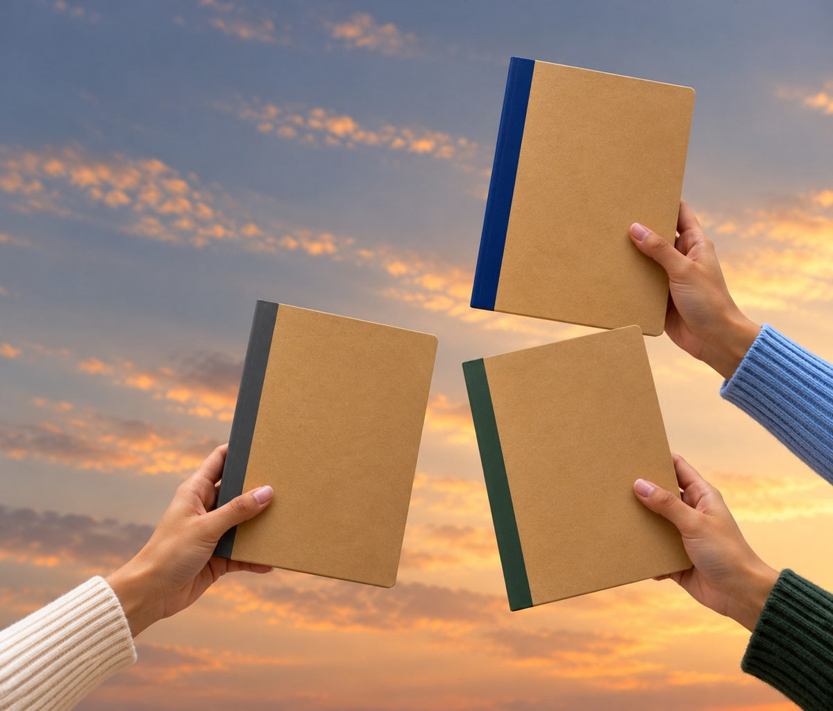 Three Zen Series notebooks held up against a sunset sky